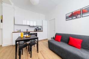Um espaço compacto com cozinha americana, área de refeições e sofá com almofadas vermelhas.