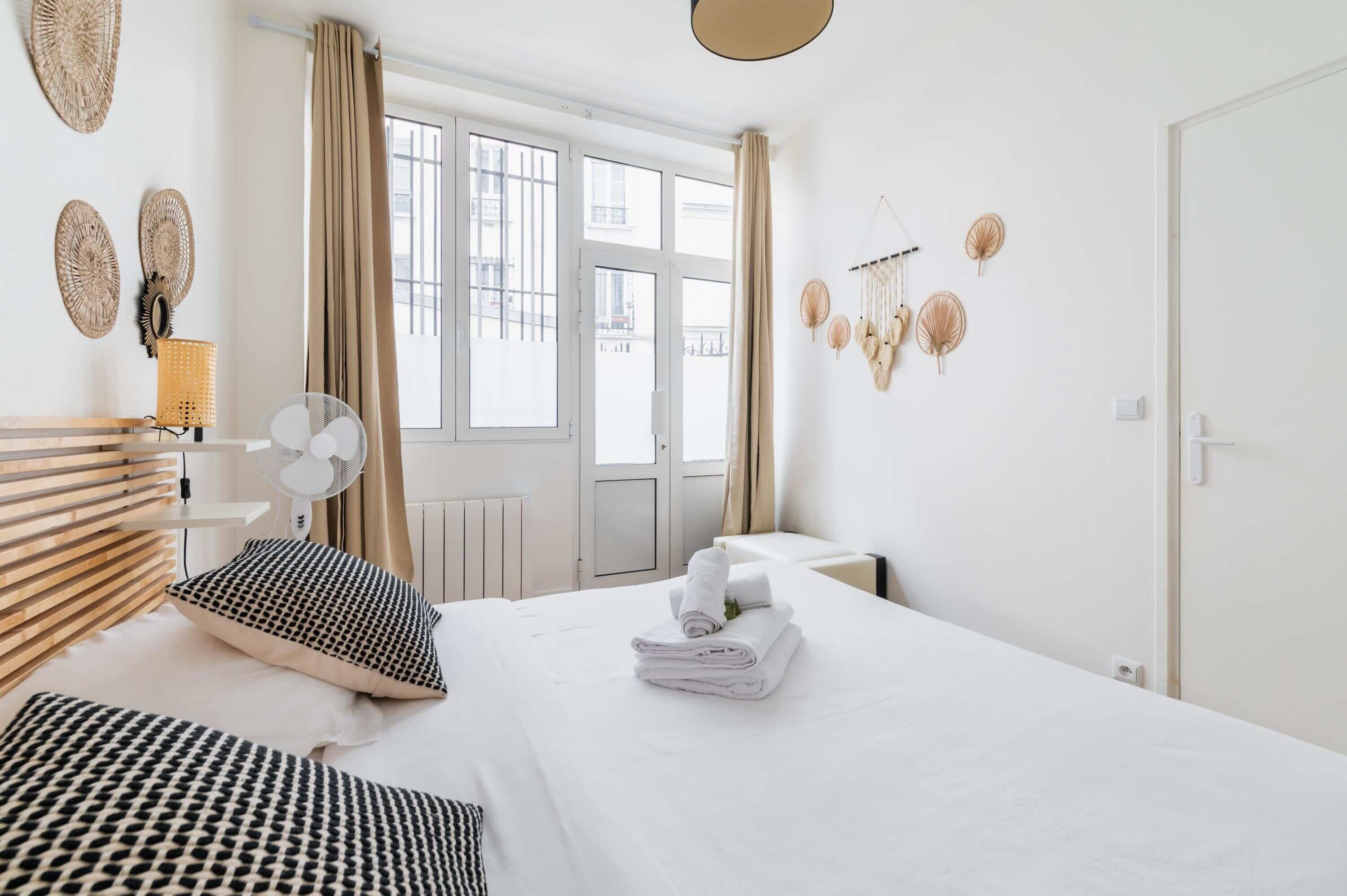 A hotel room with a bed, a fan, a window with curtains, and wall decorations.