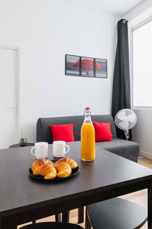 Uma mesa de jantar com croissants, um suco de laranja e duas xícaras brancas.