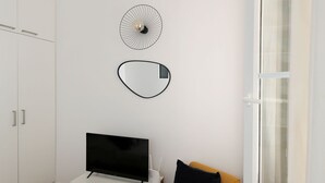 A modern room with a TV on a white stand, a yellow chair, a wardrobe, and a window with curtains. - Studio original et reposant - Paris 10 - 2P (Paris)