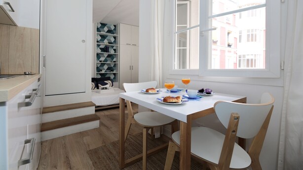 A compact kitchen with a dining area, featuring a white table, wooden chairs, and a window with a view of buildings. - Studio original et reposant - Paris 10 - 2P (Paris)