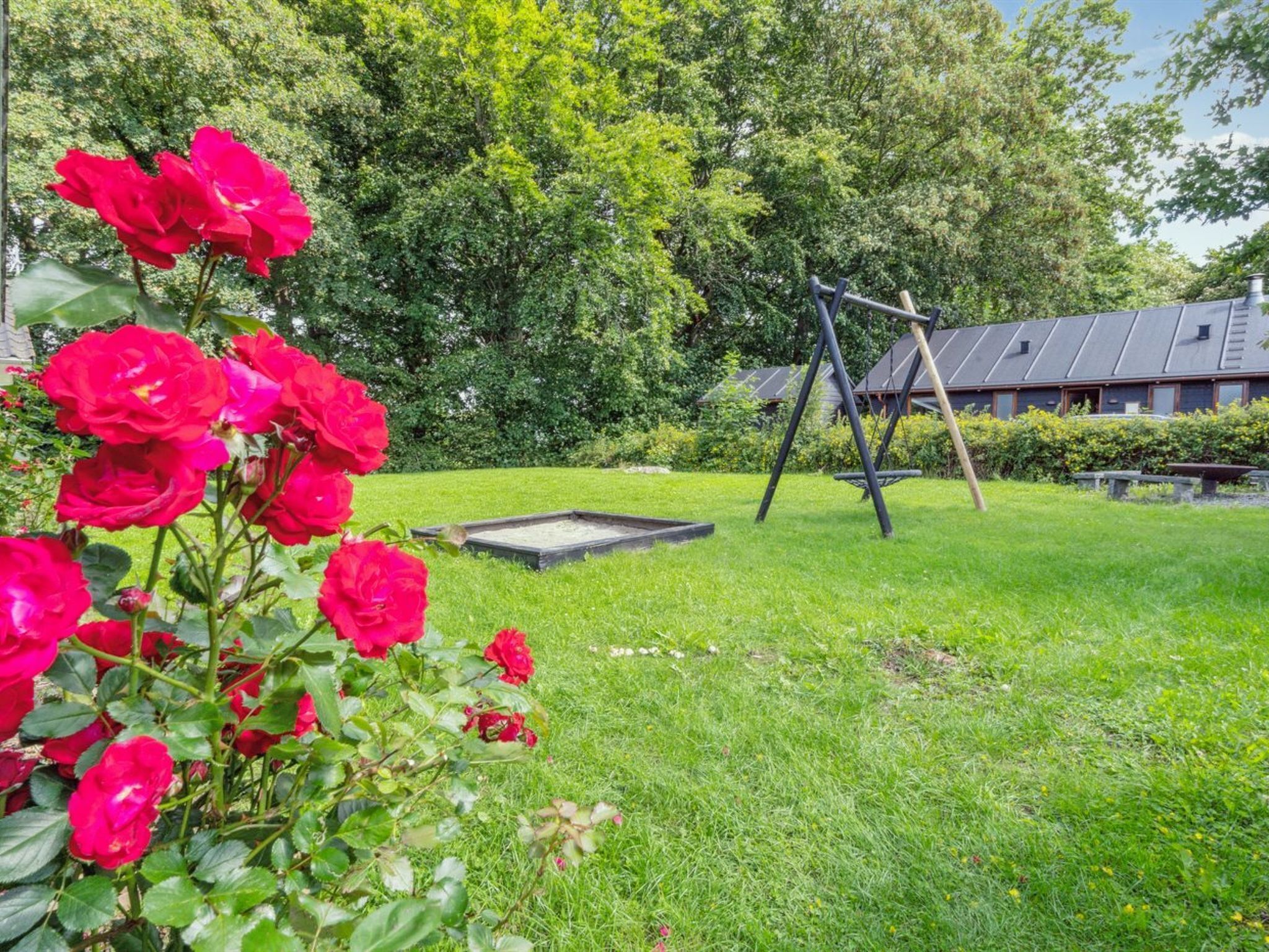 A garden with a swing set, a small pond, and a building with solar panels in the background.