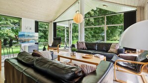 A modern living room with a leather sofa, a wooden coffee table, and a large window offering a view of greenery. - "Edin" - 150m from the sea by Interhome (Aabenraa)