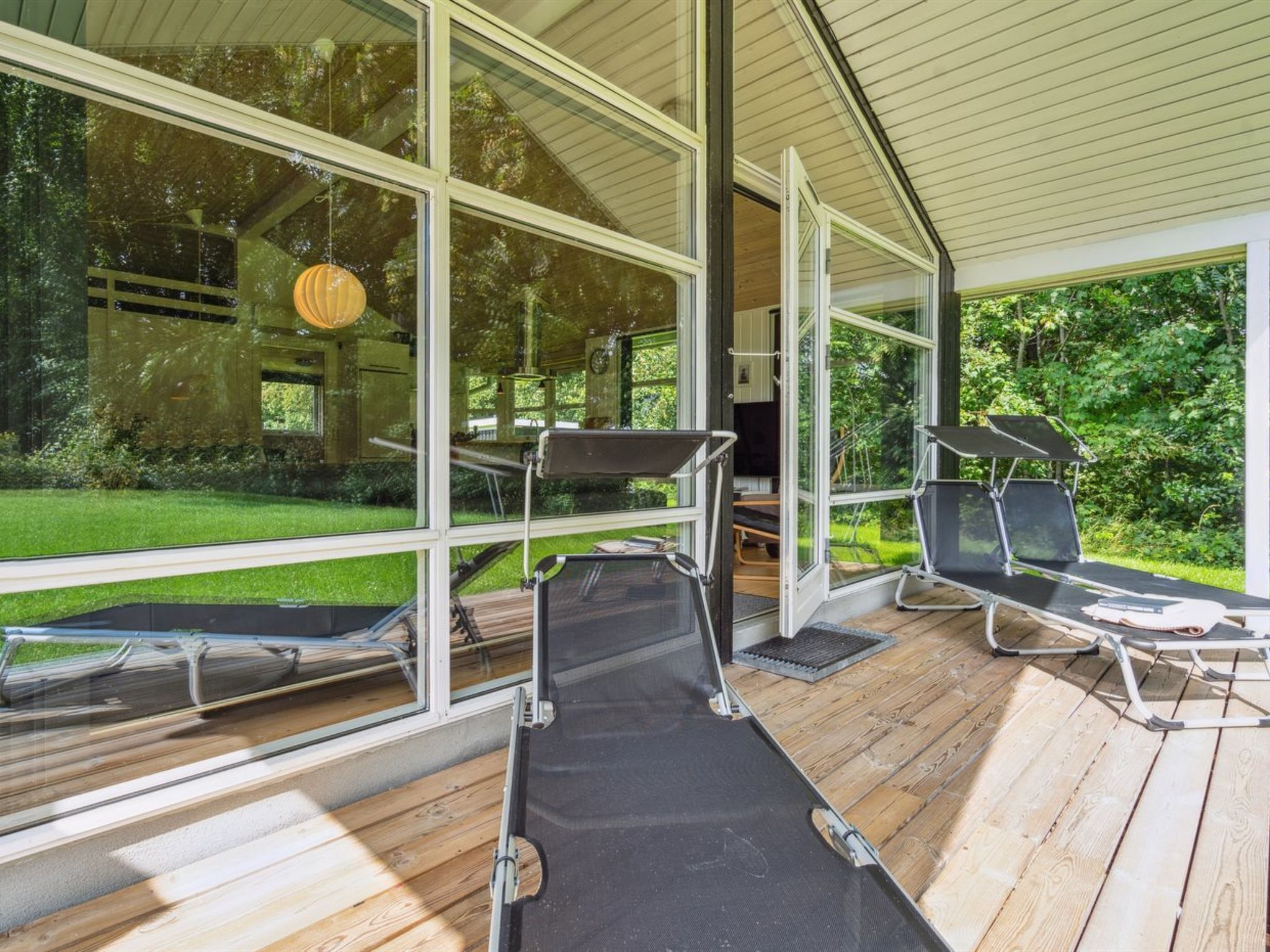 Un espace de détente extérieur moderne, doté de grandes fenêtres, d’un plancher en bois et de fauteuils noirs.