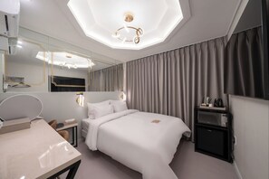 Une chambre d’hôtel moderne équipée d’un grand lit, d’une table de chevet, d’un bureau avec une chaise, d’un miroir, d’un luminaire au plafond et d’une télévision.