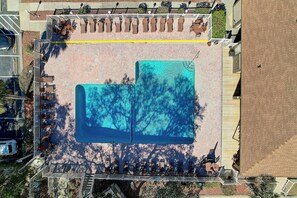 An aerial view of a swimming pool area with adjacent lounge chairs and a covered seating area.