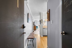 A hallway with a wooden bench, a door with a brass handle, and a kitchen area visible in the background.