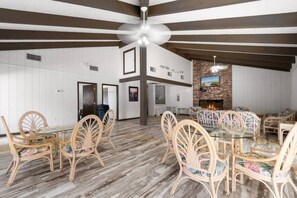 A spacious room with a high ceiling, a fireplace, and a dining area with wicker chairs and a glass table.