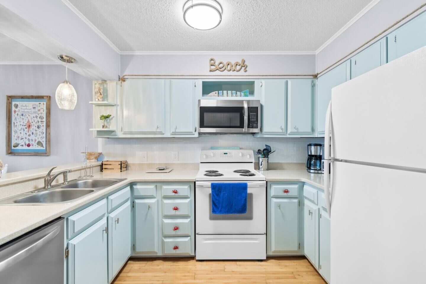 Een keuken met lichtblauwe kastjes, een witte oven, een magnetron en een koelkast.