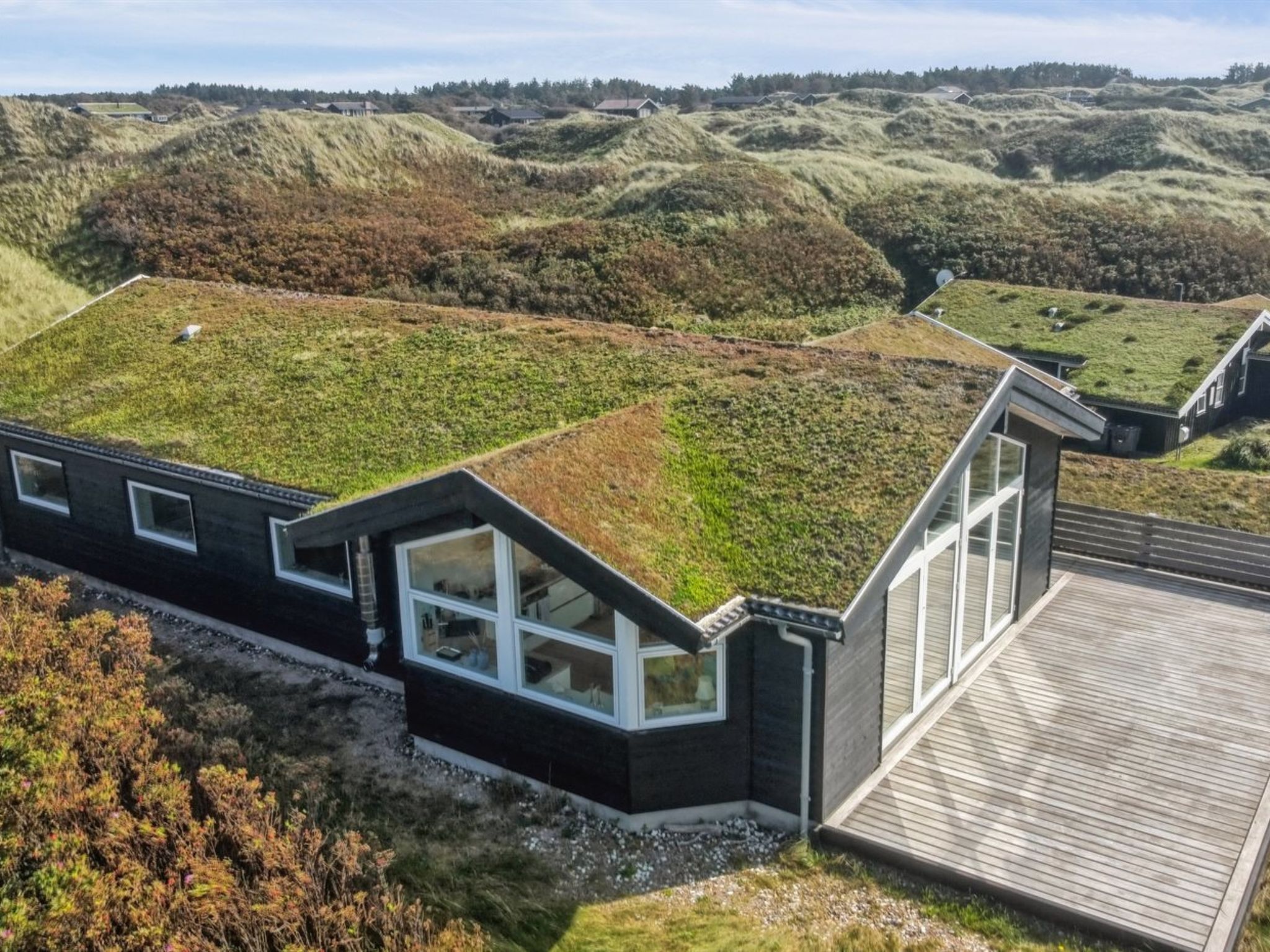 A modern house with a green roof, situated on a hillside with a view of surrounding hills.