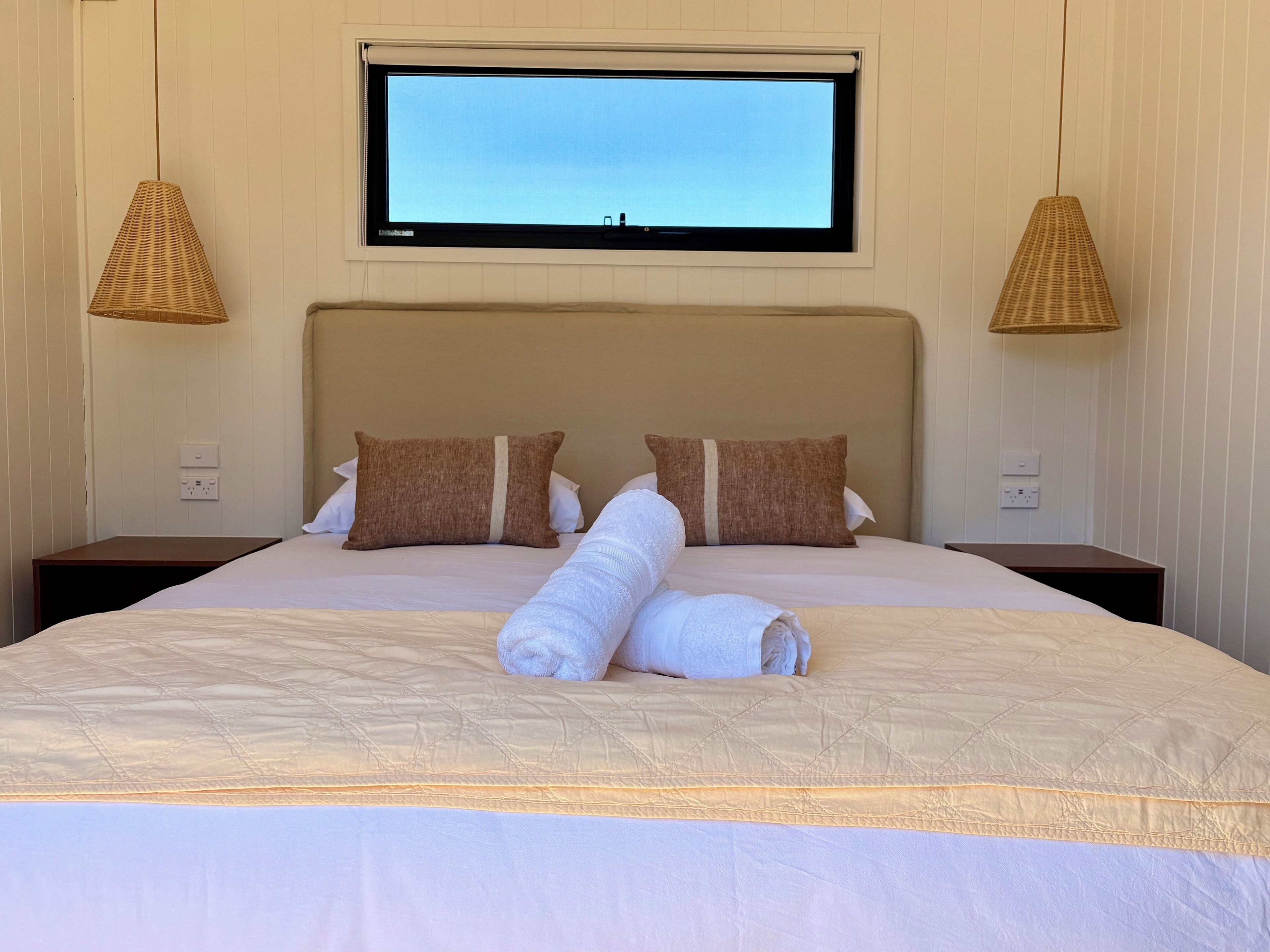 A hotel room with a large bed, two nightstands, a television mounted on the wall, and two wall-mounted lamps.