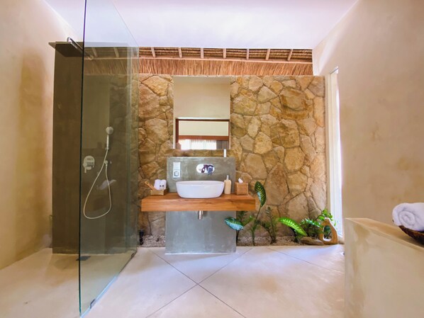 Un baño moderno con pared de piedra, cabina de ducha de vidrio, tocador de madera y un espejo grande.