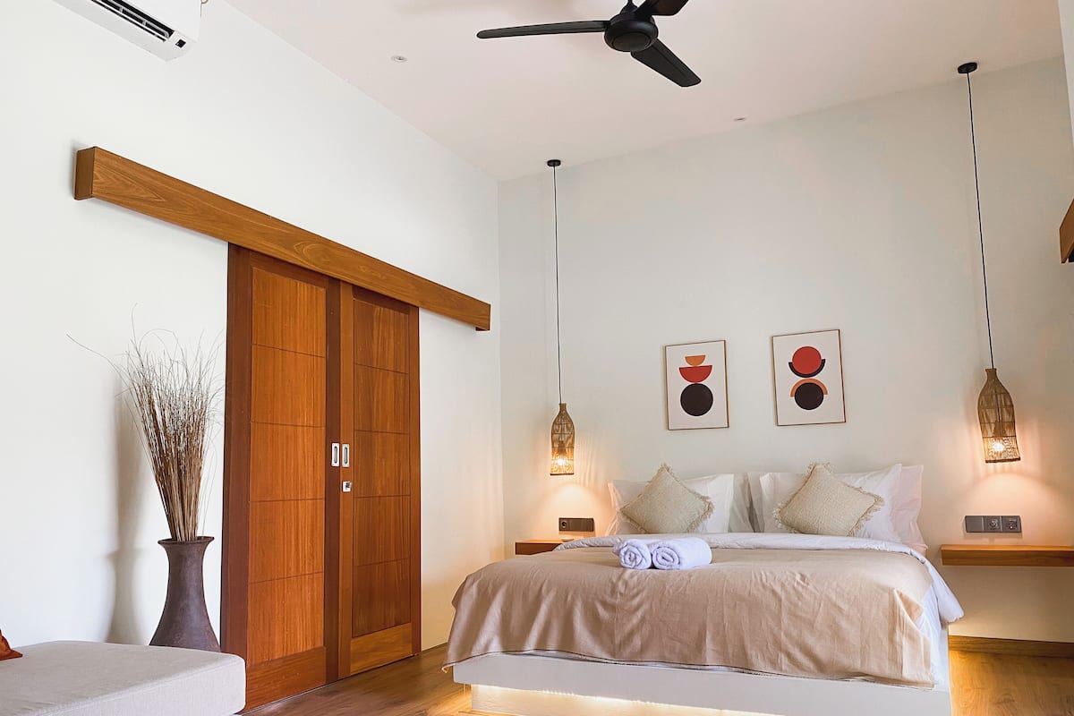 A modern bedroom with a bed, wooden wardrobe, and two wall-mounted pendant lights.