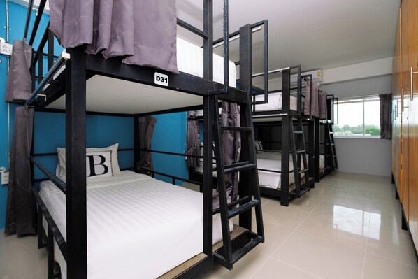 Quarto em dormitório com beliches, cada um identificado por uma letra, e uma janela com vista para o exterior.