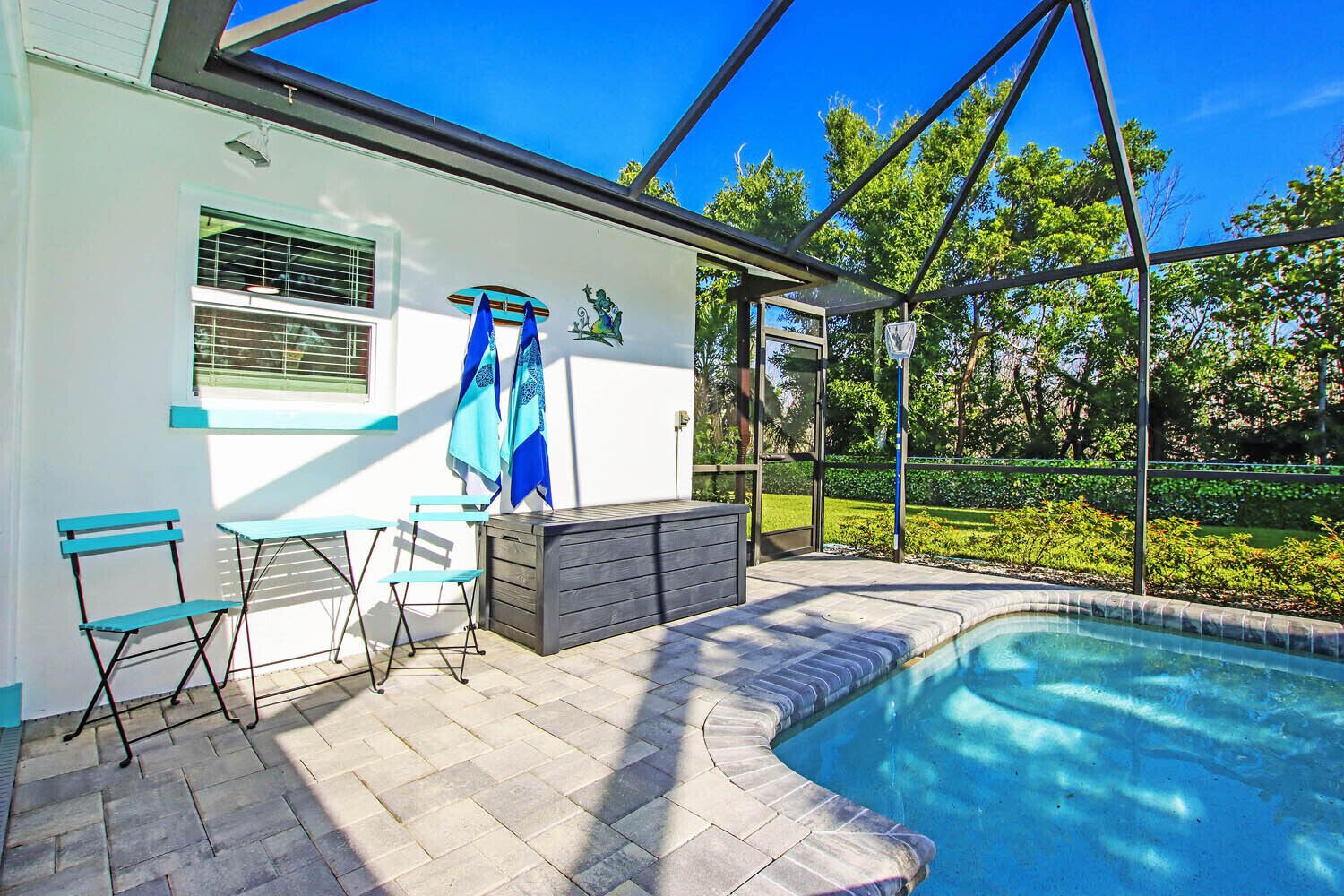A pool area with a glass enclosure, a seating area with a table and chairs, and a view of a garden.