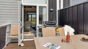 Eine Terrasse im Freien mit Grill, Korbmöbeln und einem Tisch mit Zeitschrift und Obst.