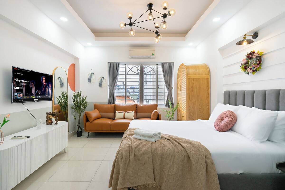 A modern hotel room with a bed, a sofa, a TV, and a desk.