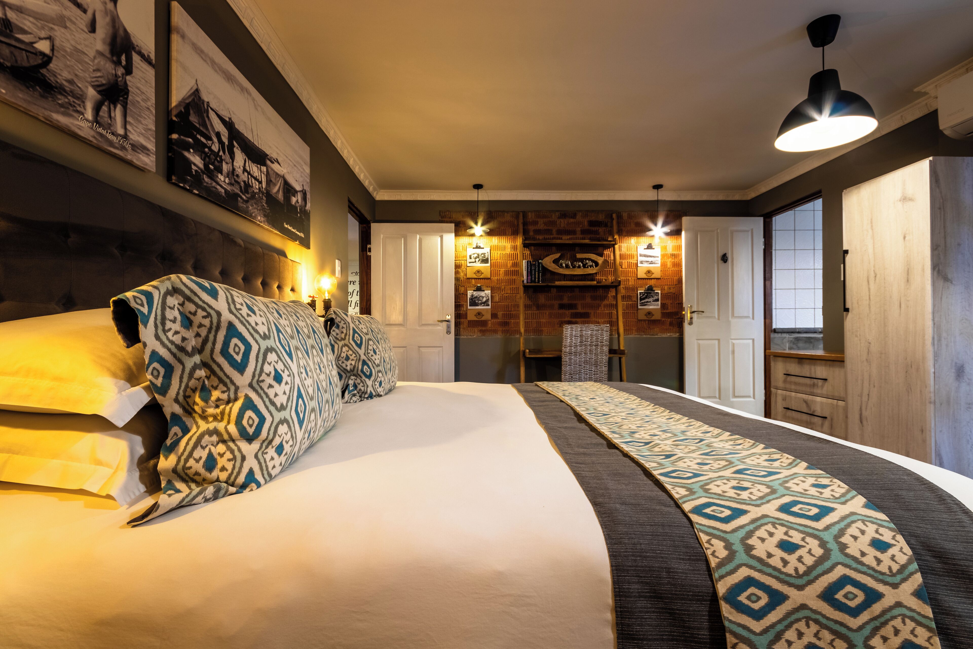 A bedroom with a large bed, patterned pillows, a headboard, and a wall-mounted shelf with books and a clock.