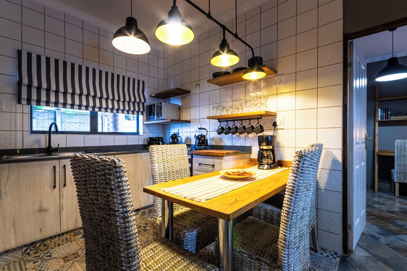 A modern kitchen with a wooden table, wicker chairs, and pendant lights.