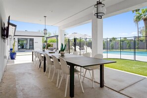 Patio esterno con tavolo e sedie, piscina e area relax coperta con ombrelloni.