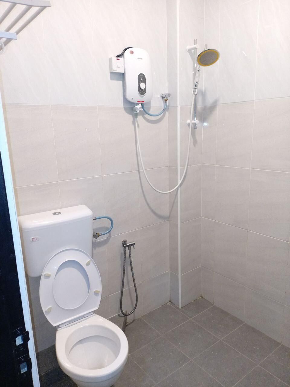 Een kleine betegelde badkamer met een toilet, een douche en een zeepdispenser op de muur.