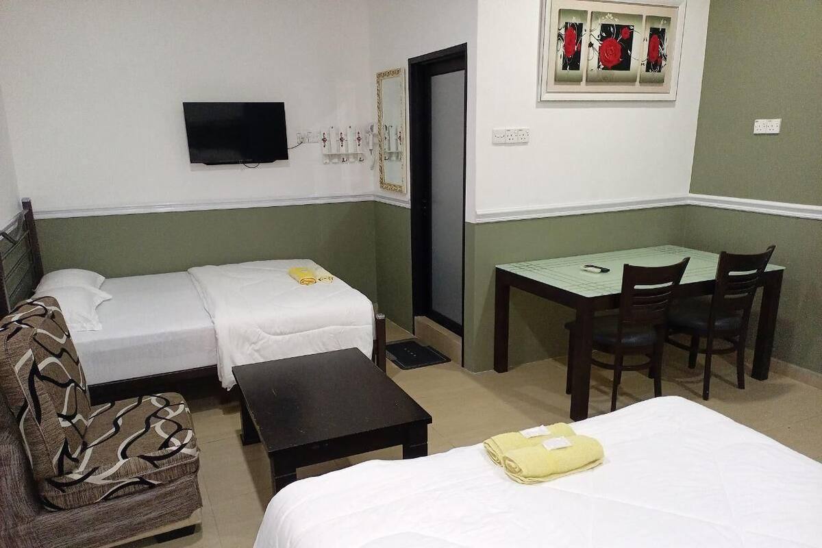 Ein Hotelzimmer mit zwei Einzelbetten, einem Schlafsofa, einem kleinen Tisch, einem Schreibtisch mit Stühlen und einem an der Wand befestigten Fernseher.