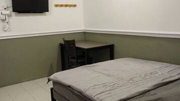 A bedroom with a bed, a chair, a small table, a wall-mounted TV, and a picture frame.
