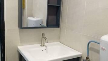 Un baño con lavamanos blanco, mueble oscuro y espejo.