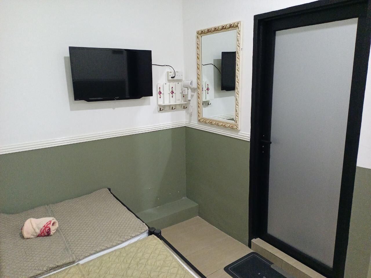 A small room with a bed, a mirror, a black TV, and a door.