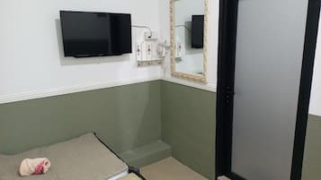 A small room with a bed, a mirror, a black TV, and a door.
