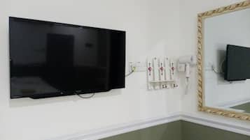 Un televisor montado en la pared, un secador de pelo y un espejo con marco decorativo.