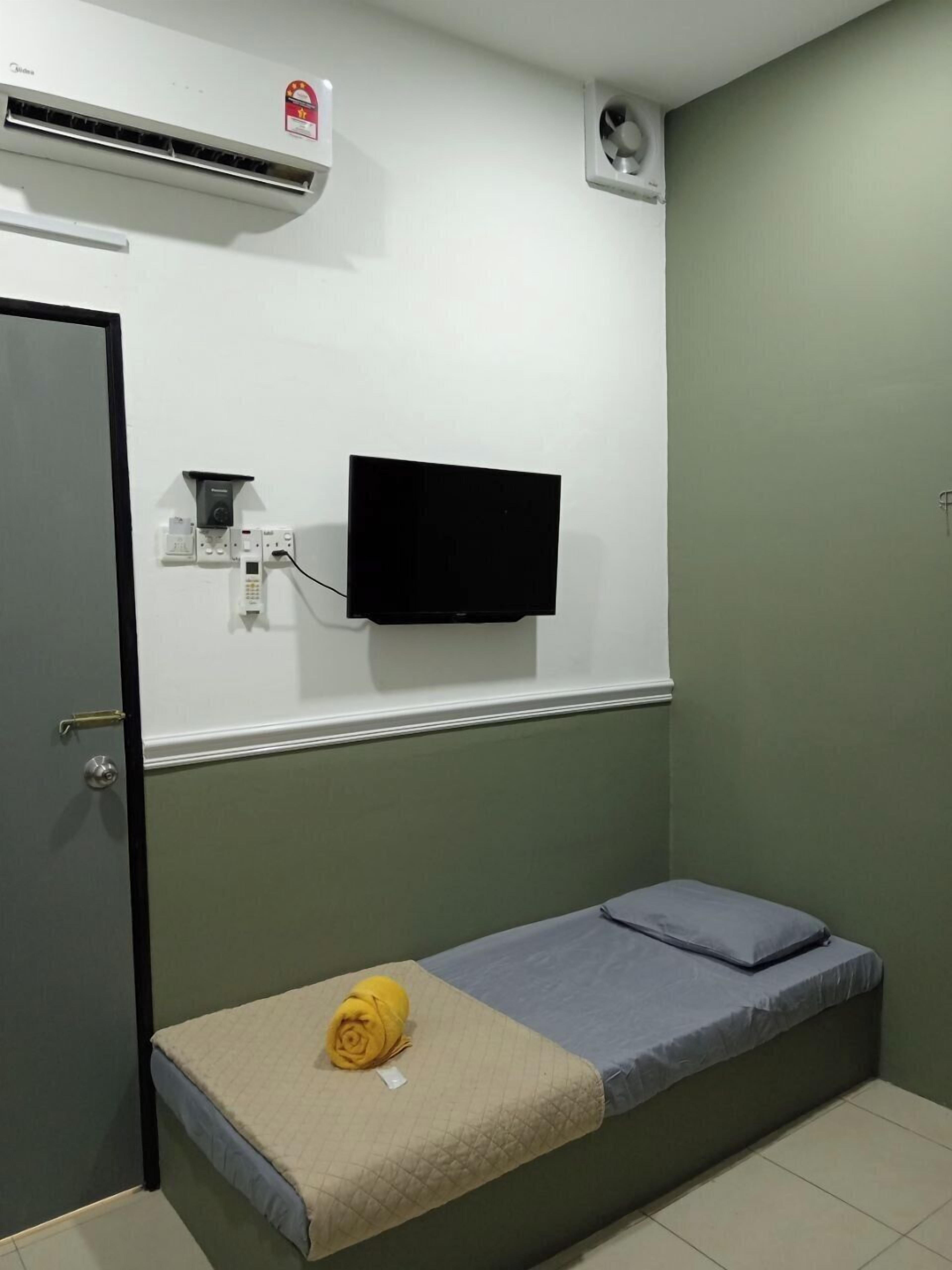 Una cama individual con colchón y almohadas, un televisor montado en la pared, un equipo de aire acondicionado y una puerta.
