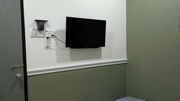 Una cama individual con colchón y almohadas, un televisor montado en la pared, un equipo de aire acondicionado y una puerta.