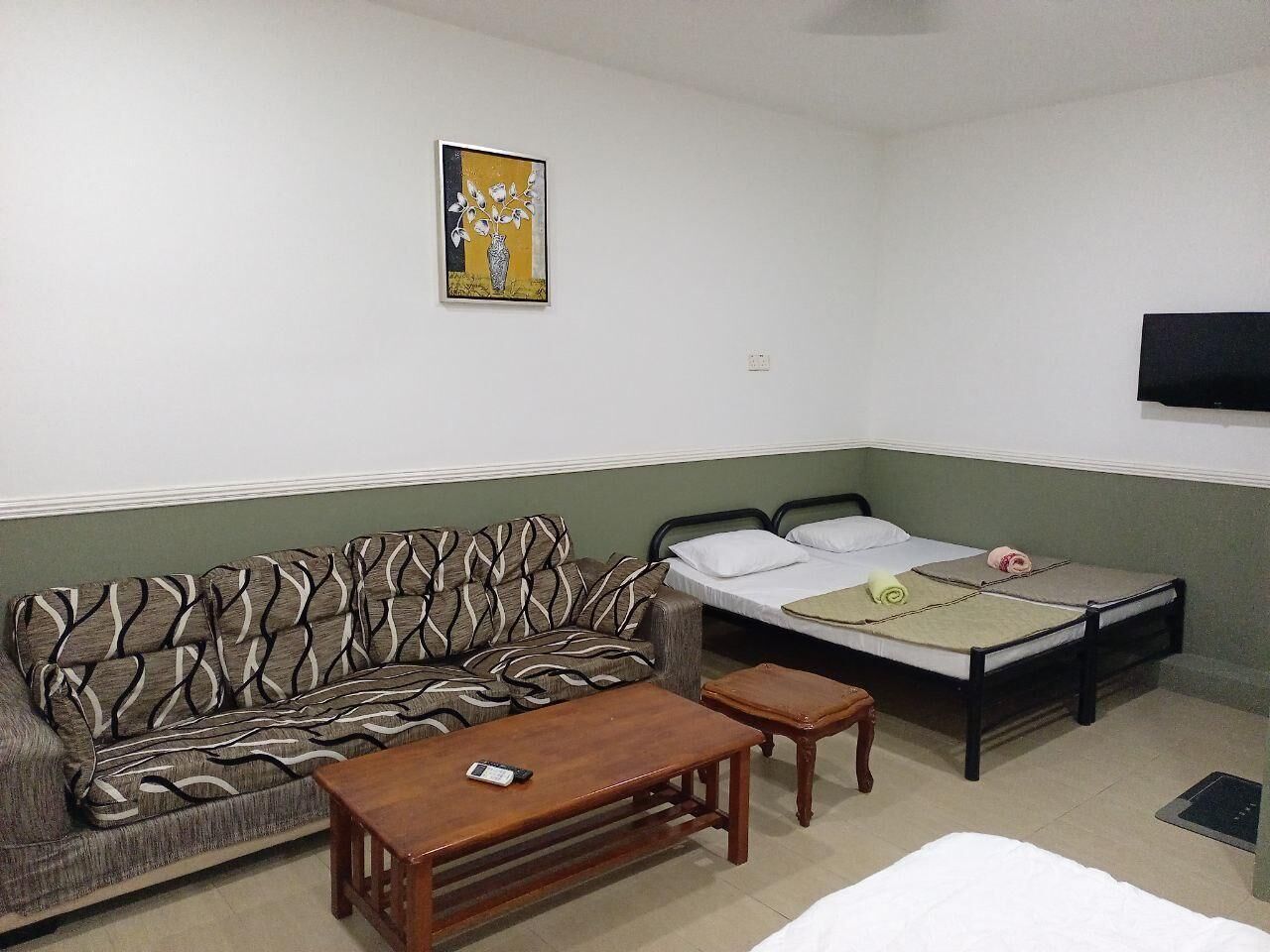 Una habitació amb un sofà, un llit, una taula petita i un televisor fixat a la paret.