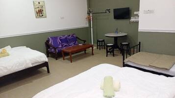 A hotel room with two single beds, a sofa, a small round table, and a TV mounted on the wall.