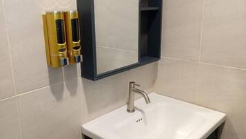 Een badkamer met een witte wastafel, een donkere kast, een spiegel en twee gouden zeepdispensers.
