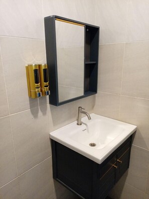 Un bagno con un lavandino bianco, un mobile scuro, uno specchio e due erogatori di sapone dorati.