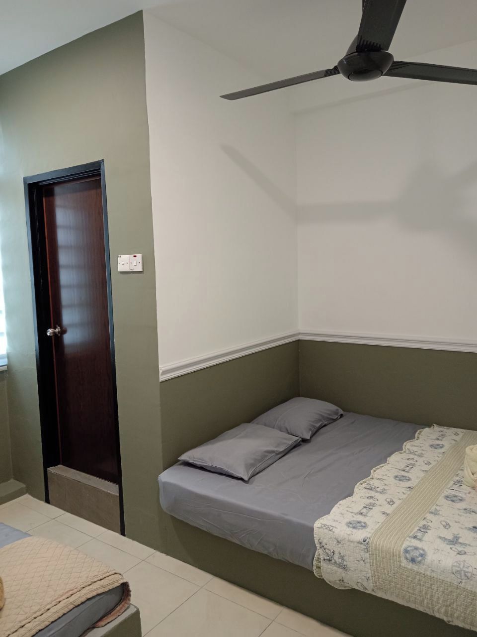 A single bed with a grey mattress and pillows, a ceiling fan, a door, and a light switch on the wall.