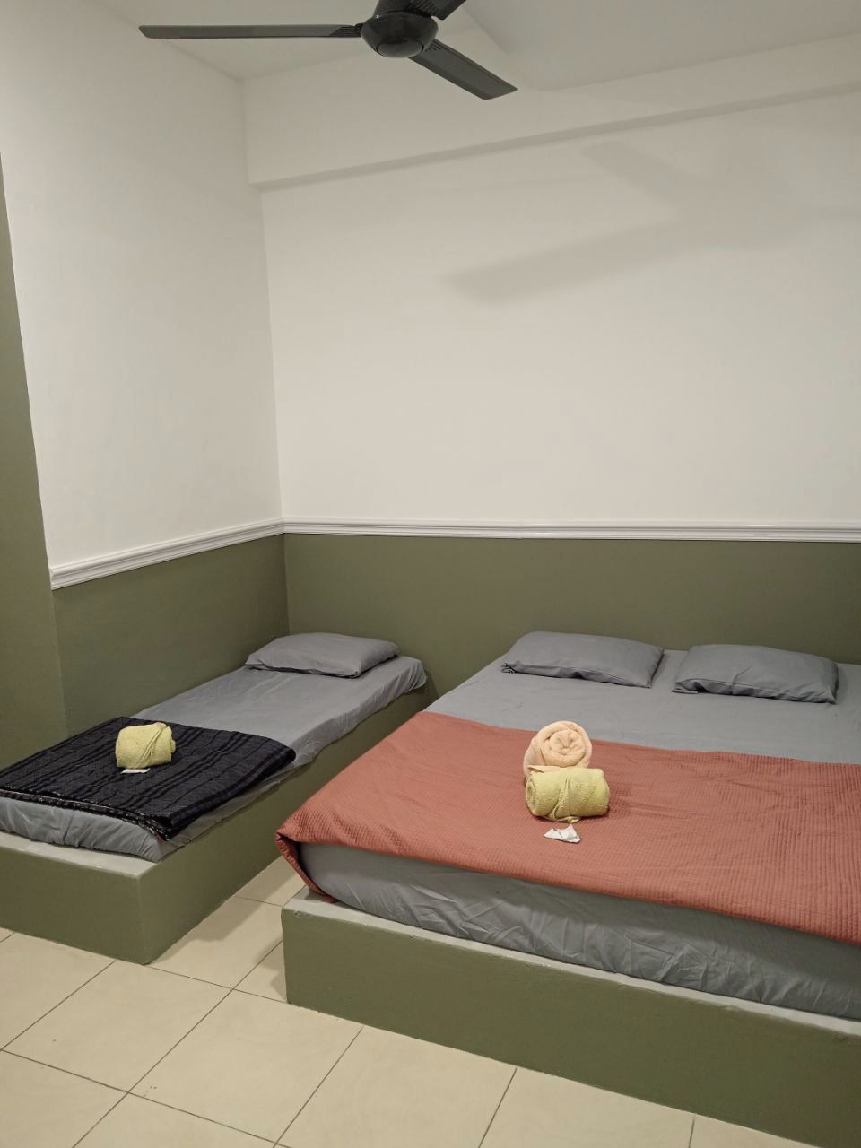Una habitación con dos camas individuales, ventilador de techo y una pared de acento verde.