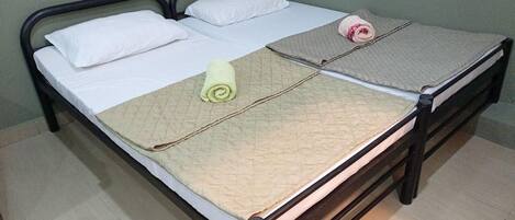 A double bed with a quilt, pillows, and a rolled towel.
