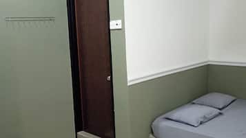 A small, single-room accommodation with a bed, a door, and a wall-mounted shelf.