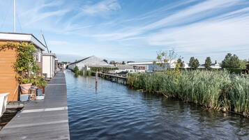 A canal-side walkway with a wooden dock, a greenhouse, and a row of houses.