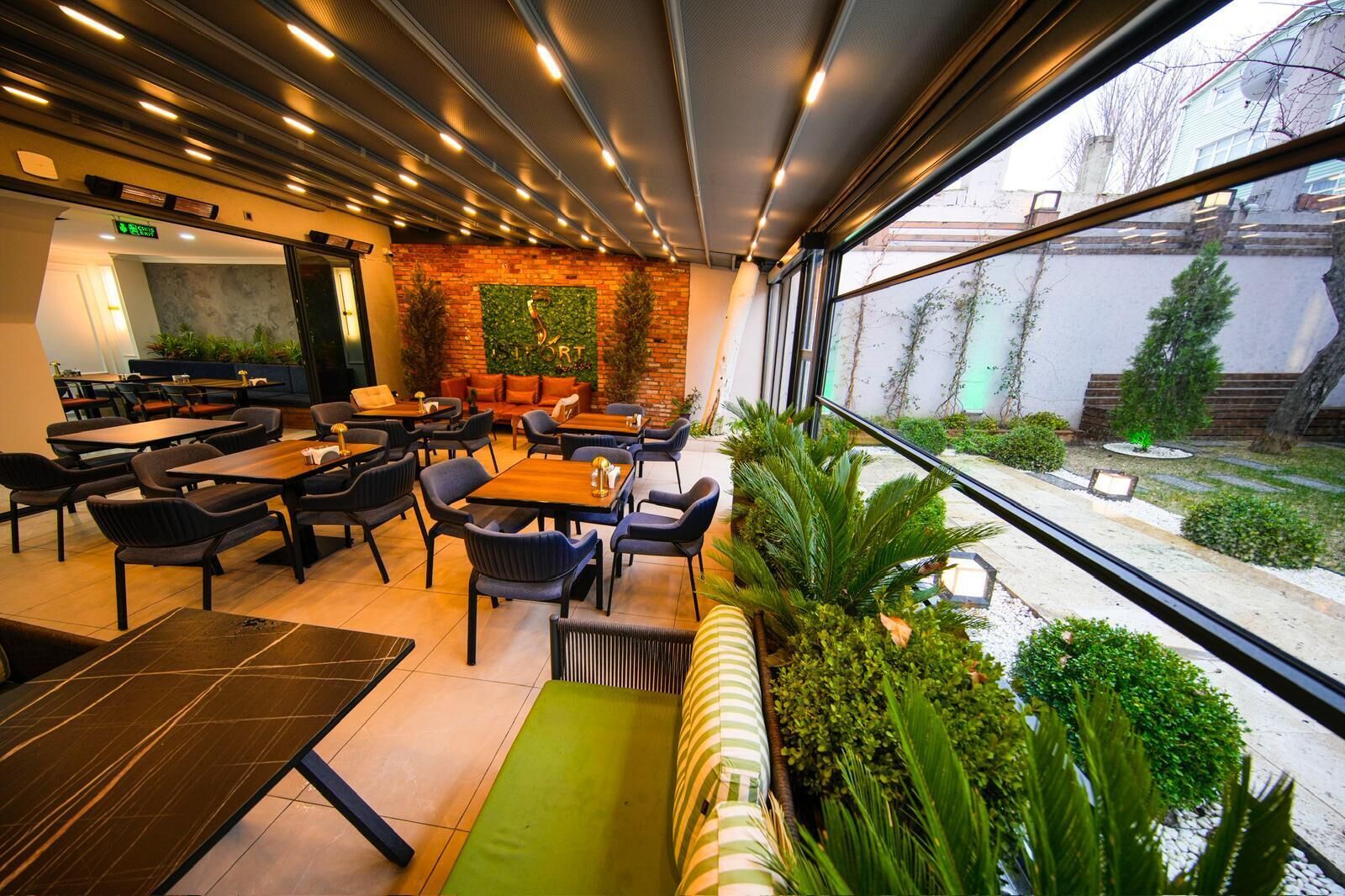 A modern restaurant with indoor seating, a brick accent wall, and a view of the outside.