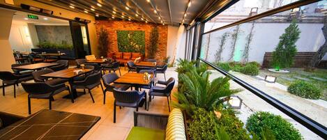 A modern restaurant with indoor seating, a brick accent wall, and a view of the outside.