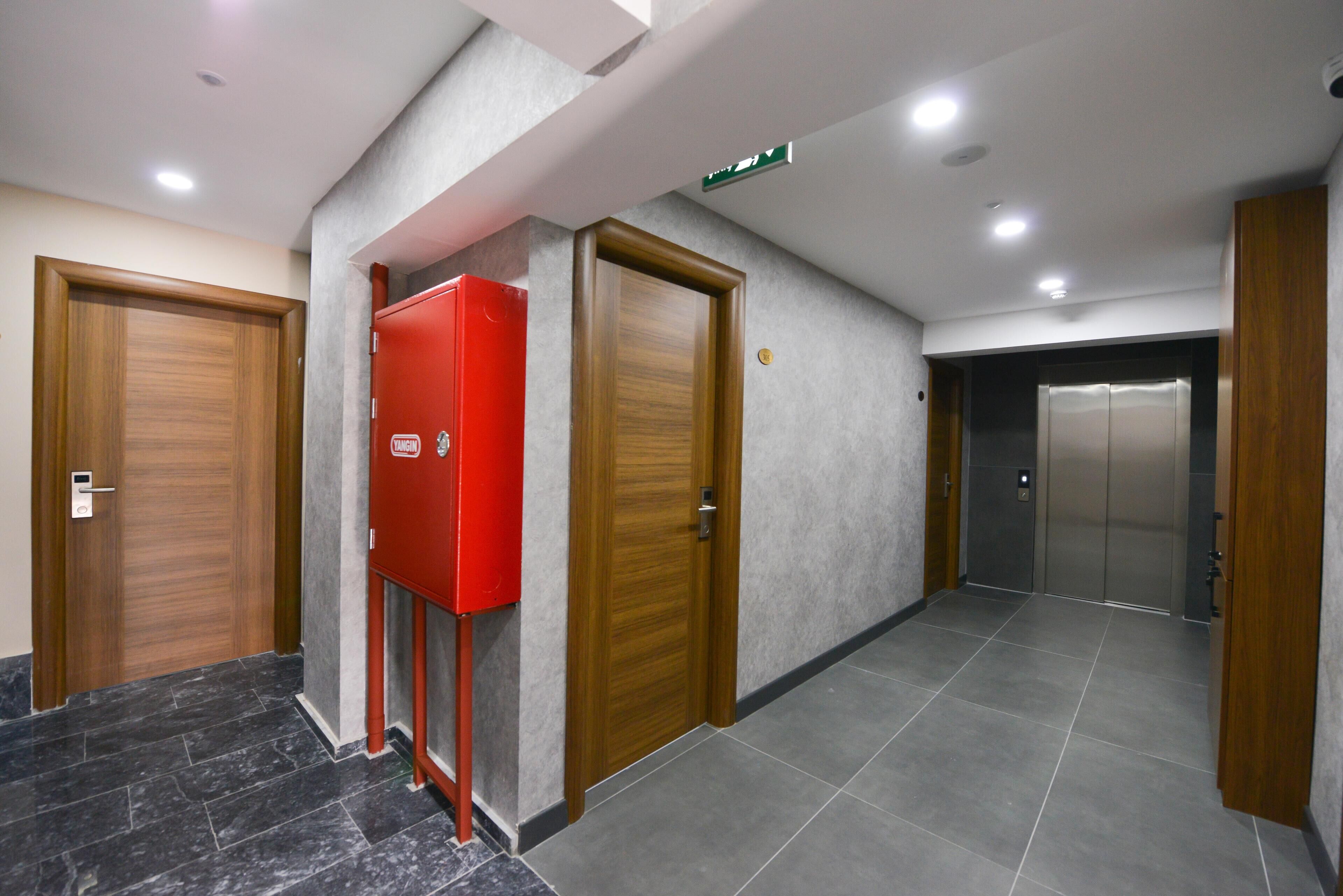 Un pasillo con dos puertas de madera, una caja roja de alarma contra incendios y un ascensor.