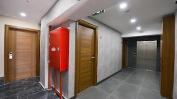 Un pasillo con dos puertas de madera, una caja roja de alarma contra incendios y un ascensor.