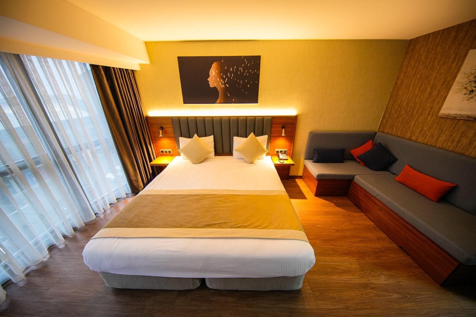 Quarto de hotel com uma cama grande, um sofá, um quadro na parede e vista pela janela.