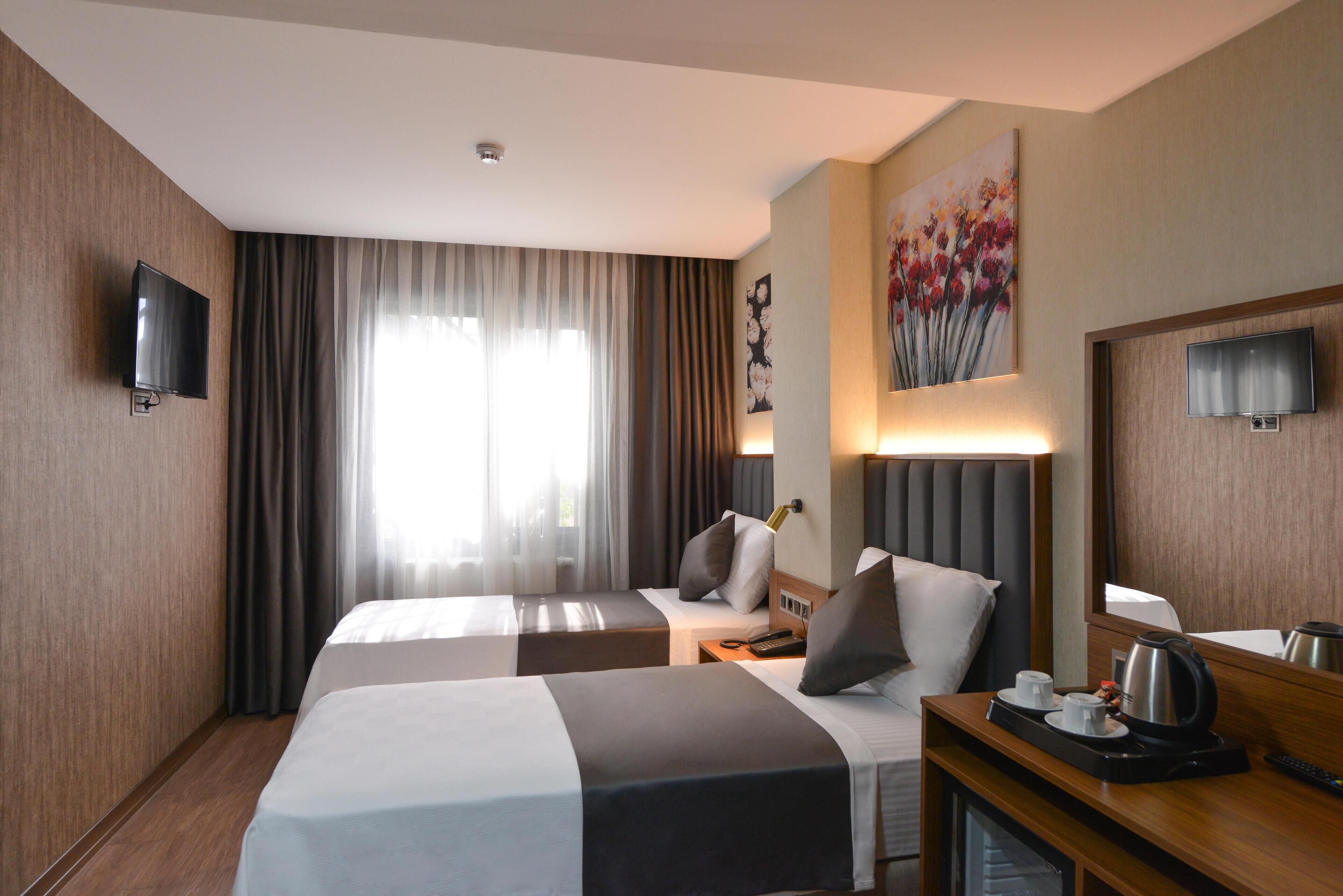 Habitación de hotel con dos camas, un televisor de pantalla plana, un cuadro, un minibar y un ventanal grande con cortinas.