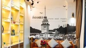 A modern living room with a sofa, two armchairs, a coffee table, and a bookshelf. A large wall mural of Istanbul's skyline is visible. - Istport Garden (Arnavutköy)