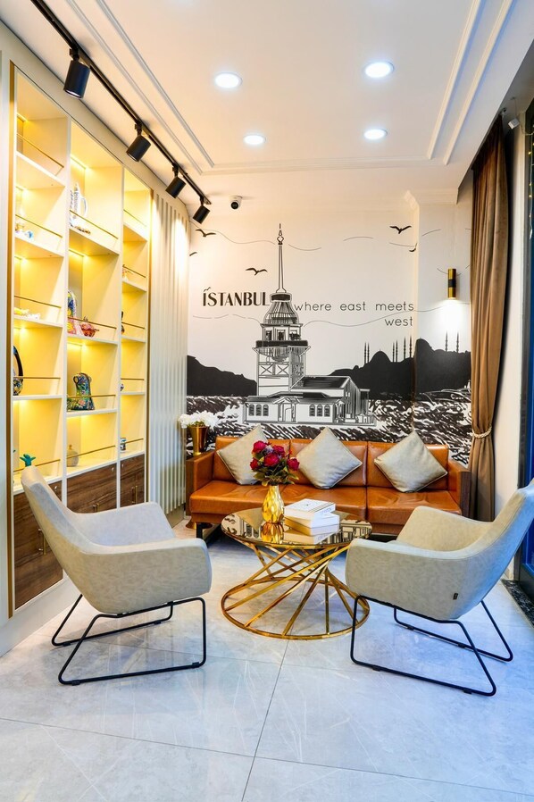 Un salon moderne comprenant un canapé, deux fauteuils, une table basse et une bibliothèque. Un grand tableau mural représentant le panorama d’Istanbul est visible.